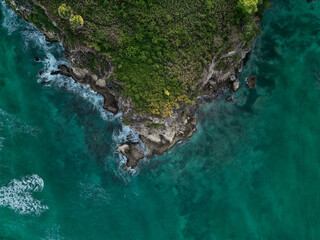 Aerial. Dark turquoise water with white foamy waves and green rocky shore