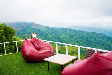 Red bean bags and a coffee table on the terrace with a mountain background, the view of Doi Chang, Chiang Rai, Thailand - obrazy, fototapety, plakaty