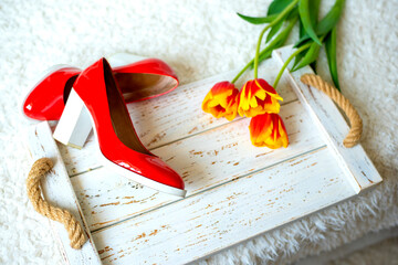 scarlet heeled shoes and red tulips on a white vintage wooden background.