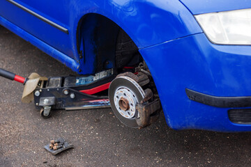 A wheel is removed from a blue car