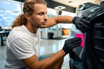 Man uses pink spatula to apply anti-gravel film to car body