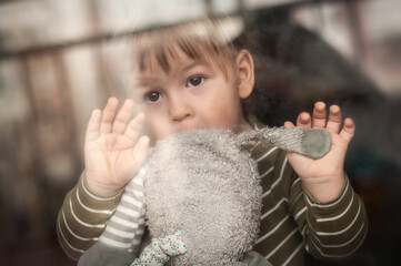 Portrait of cute baby boy with stuffed toy looking out window, looking sad. Love and family emotion