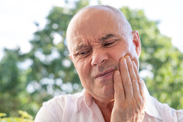 senior, caucasian man holds on to jaw, close up male face with facial expression suffering,...