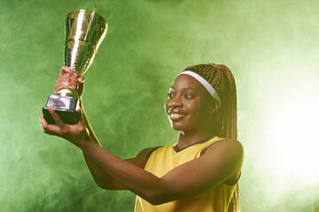 Waist up portrait of smiling African American female athlete holding trophy cup and celebrating...