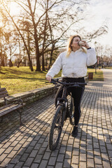 Woman Enjoying a Refreshing Drink While Cycling in a Sunny Park
