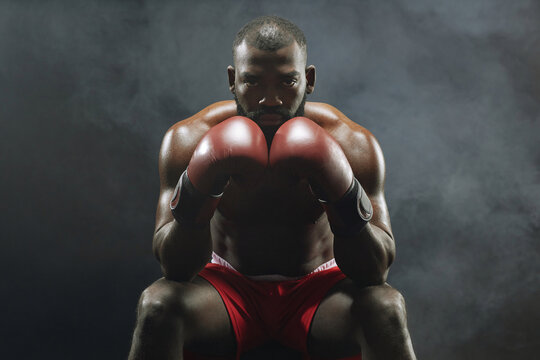 Dramatic front view portrait of muscular African American boxer looking at camera intensely with smoke in background