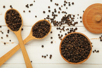 Black peppercorns in wooden bowl and spoon on white wooden background.