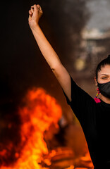 retrato de mujer con el brazo arriba en señal de protesta con llamas de fondo 
