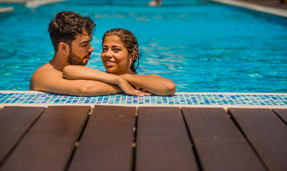 retrato de pareja joven latina en la piscina del hotel en vacaciones sonriendo - obrazy, fototapety, plakaty