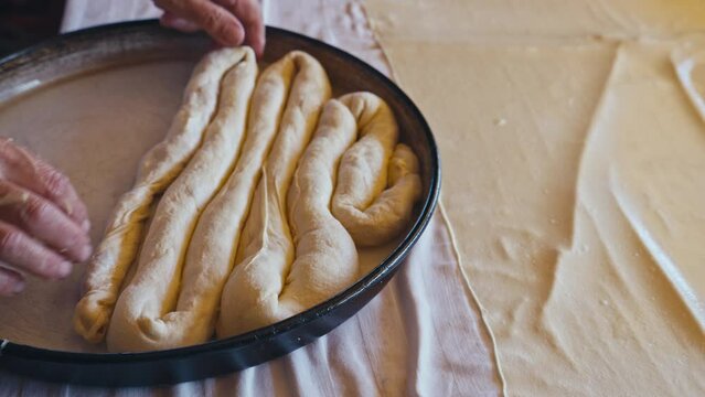 Close-up of old female hands preparing traditional Bosnian and Turkish Borek in the metal baking tray. This dish is featuring savory fillings like cheese, meat, or potato wrapped in flaky filo pastry