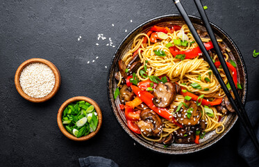 Vegan stir fry noodles with red paprika, champignons, green onion and sesame seeds with ginger, garlic and soy sauce.. Black table background, top view
