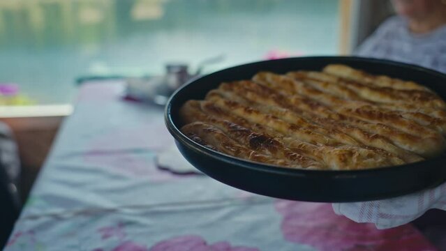 Close-up of serving traditional stuffed Bosnian and Turkish Dish in the metal baking tray onto the table. This dish features savory fillings like cheese, meat, or potato wrapped in flaky filo pastry