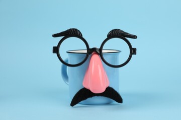 Man's face made of cup, fake mustache, nose and glasses on light blue background