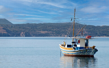 A traditional fishing boat "kaiki" lays in the calm sea under a clear blue sky. Summer travel in Greece.