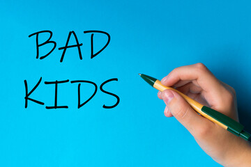 Children hand with pen write on an blue white background. Writing hand. Word Bad kids