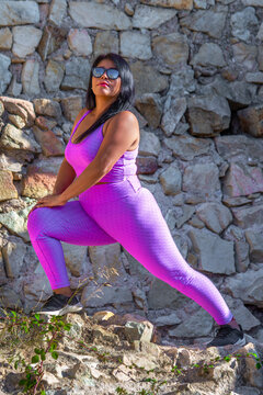 Sexy fat latin woman with positive and self-confident attitude, wearing tight pink sportswear, stretching her legs with her arms resting on her knees in the field.