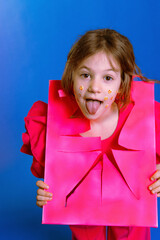 girl in a pink suit looks through the frame, little girl shows her tongue