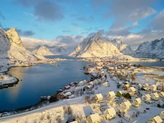 Fotobehang Aerial view of Lofoten island Norway. The winter season of sunrise fishing village of Reine with snowscape mountain peak reflect on water. Norway with red rorbu houses. With falling snow in winter. © ultramansk