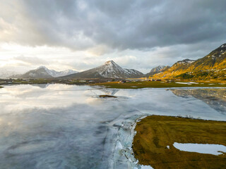 Panoramic view of beautiful white winter wonderland scenery with snowy mountain summits reflecting in crystal clear ice lake on a cold sunny day with sky and clouds. Norwegian fjords mountain.
