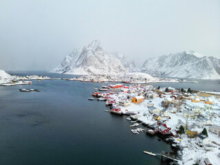 Top aerial view Beautiful landscape of snowy mountain and fishing village on the coastline in winter at Lofoten Islands. Norway with red rorbu houses in winte