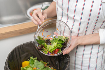 Compost from leftover food asian young housekeeper woman, female hand holding salad bowl use fork scraping waste, rotten vegetable throwing away into garbage, trash or bin. Environmentally responsible
