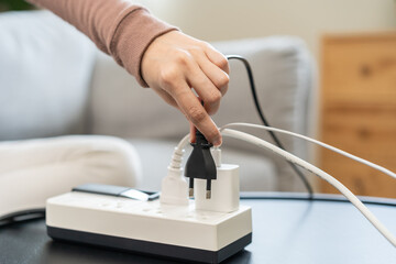 Closed up hand of woman plugged in, unplugged electricity cord cable on socket on table for energy saving, electric power on plate outlet, control expense electrical appliances, environment concept. - obrazy, fototapety, plakaty