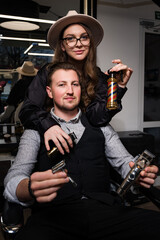 Barber boy and girl are holding tools with barbershop attributes sitting on a chair in the salon.