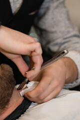 A barber shaves the neck of a bearded customer with dangerous razor. Shaving the contour of the beard for the correct shape.