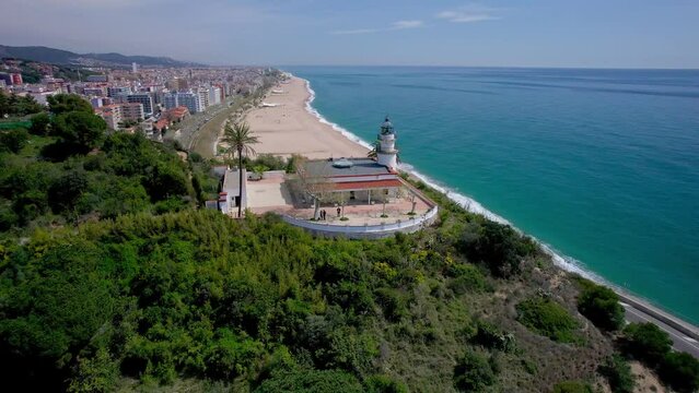 Vídeo aéreo con dron de un faro sobre una montaña frente a una playa. Hermosa vista del mar y balneario de la costa de Barcelona