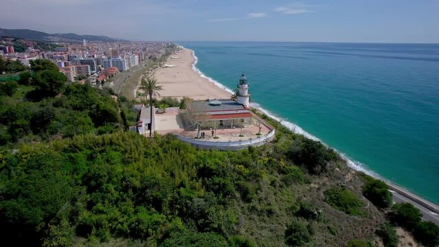 V&iacute;deo a&eacute;reo con dron de un faro sobre una monta&ntilde;a frente a una playa. Hermosa vista del mar y balneario de la costa de Barcelona