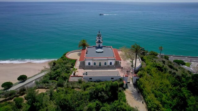 V&iacute;deo a&eacute;reo con dron de un faro sobre una monta&ntilde;a frente a una playa. Hermosa vista del mar y balneario de la costa de Barcelona