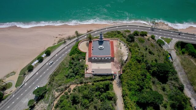 V&iacute;deo a&eacute;reo con dron de un faro sobre una monta&ntilde;a frente a una playa. Hermosa vista del mar y balneario de la costa de Barcelona
