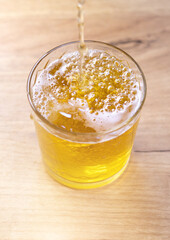 Pouring liquid gold-yellow beer with white foam into a glass. Close up view.