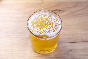 Pouring liquid gold-yellow beer with white foam into a glass. Close up view.