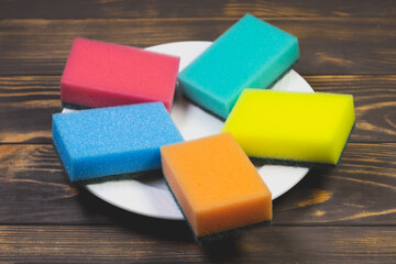 Colorful sponges for washing dishes on the white plate. Things for kitchen house cleaning.