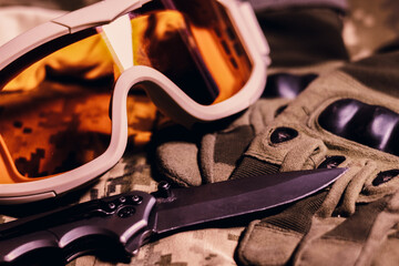 Fototapeta na wymiar Tactical military gloves, helmet, glasses and knife on the khaki camouflage uniform. Soldier ammunition.