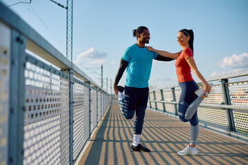 Happy athletic couple stretching their legs while exercising together outdoors.