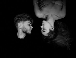 An overhead view of a man and woman lying together on a dark background and looking at each other....