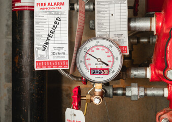 Building fire sprinkler system with inspection tags in water meter room. Close up of water gauge and pipes. Defocused winterized label for parkade fire sprinklers system protection. Selective focus.