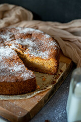 sponge cake with sugar on top on a dark background. The sponge cake is started with a cut piece of sponge cake. A pitcher of milk and jam is peeking out. Perfect for breakfasts or snacks.