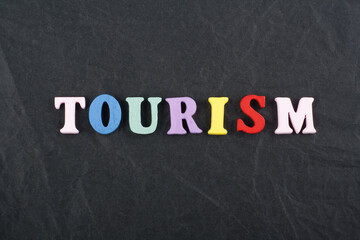 Obraz premium TOURISM word on black board background composed from colorful abc alphabet block wooden letters, copy space for ad text. Learning english concept.