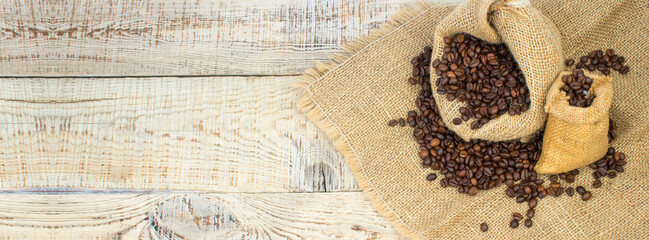 Opened burlap bags, a cup of coffee, scattered whole coffee beans on a white background. Banner.