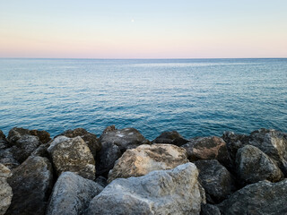 Fototapeta na wymiar Rippled empty sea, purple, pink, blue sky background texture. Afternoon at rocky beach, copy space.