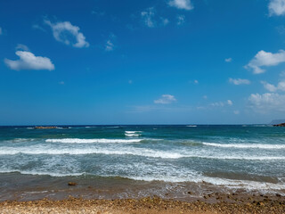 Summer holiday in Greece, ripple sea, white foam wets pebble beach, blue sky copy space. Ad template