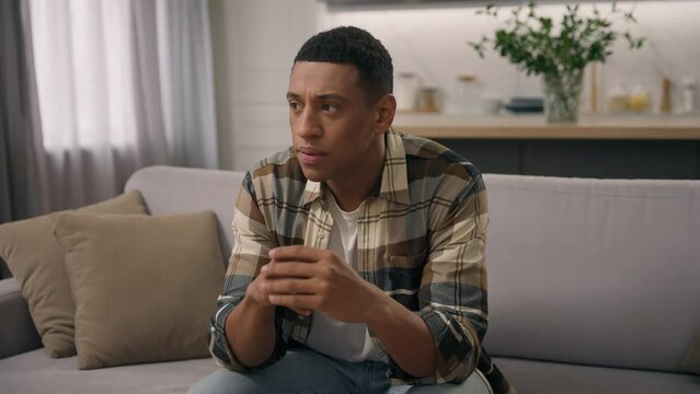 Pensive African American ethnic man homeowner worry about loan mortgage thoughtful hesitate male guy thinking rubbing hands ponder idea solution ponder think doubtful puzzled decide at home sofa couch