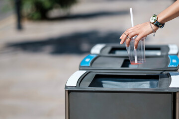 Woman hand throwing away a cup in the bin outdoors.