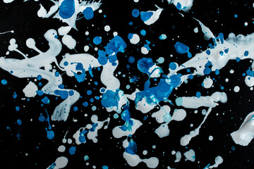 White and blue paint splatter scattered on black background, abstract texture