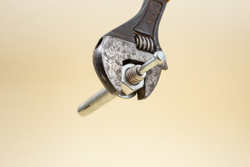Adjustable wrench tightening a screw on beige background, soft focus close up