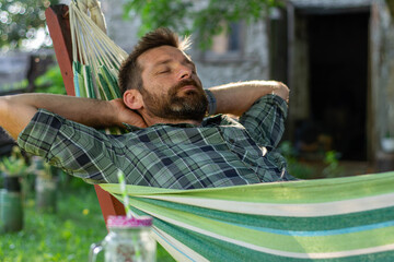 man drinking on hammock fresh juice ,A man is resting in a hammock in a country house .A young guy lies in a hammock, dozing outdoors in the summer in the green of trees in the country
