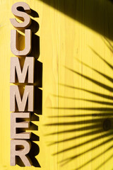 Composition created with letters forming the word summer at the edge of the composition with yellow background and palm tree shadow
